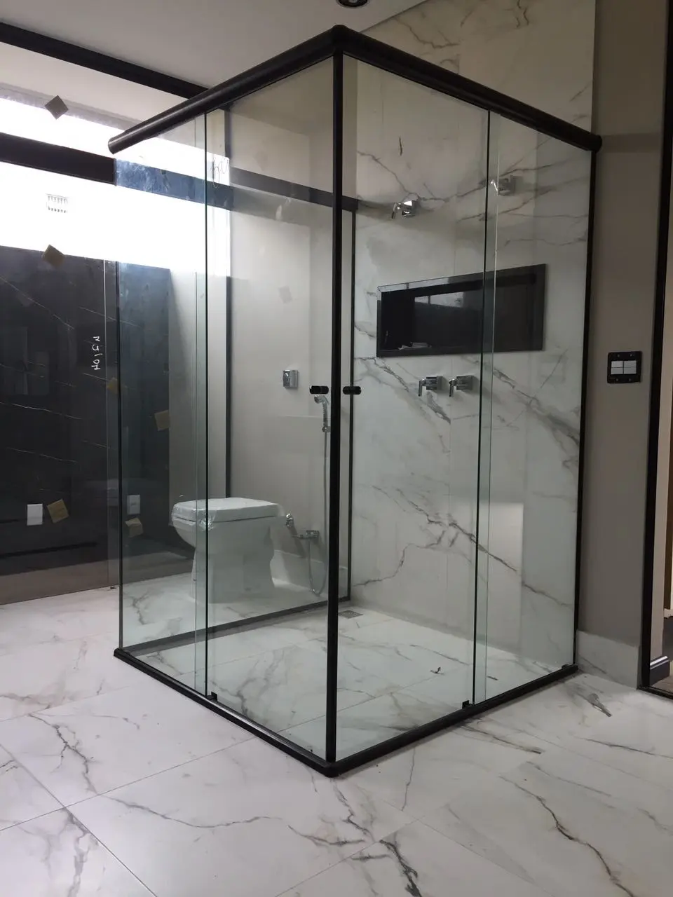 Box de vidro com perfil preto em banheiro de mármore, com ducha embutida